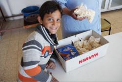 Um Hassan's grandson watches as she prepares a box of homemade muffins and popcorn to deliver to village kindergarten